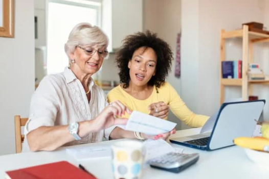 Older woman and a younger woman sitting at a table, in front of a laptop, paying a bill