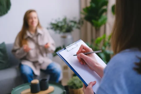 Someone sitting down taking notes while speaking with a woman sitting on a couch