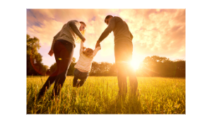 Young man and woman with their back to the camera, swinging their small child in the sunshine